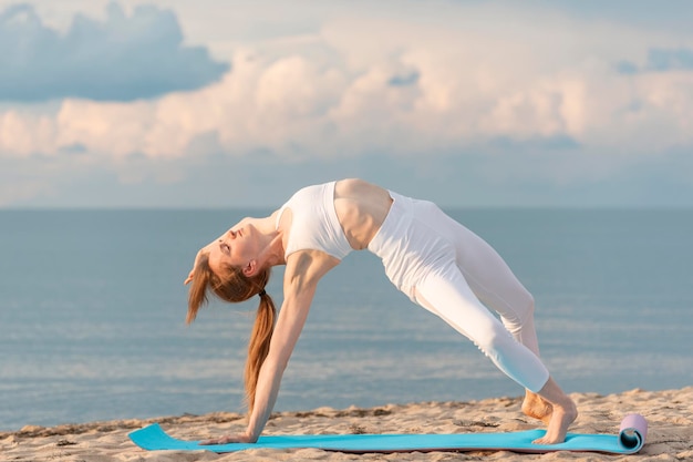 Jovem mulher saudável praticando ioga no fundo do mar Garota magra fazendo ioga na praia