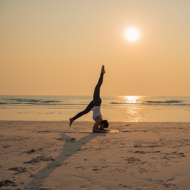 Jovem mulher saudável Yoga praticando yoga pose na praia ao nascer do sol