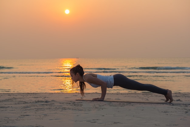 Jovem mulher saudável Yoga praticando yoga pose na praia ao nascer do sol