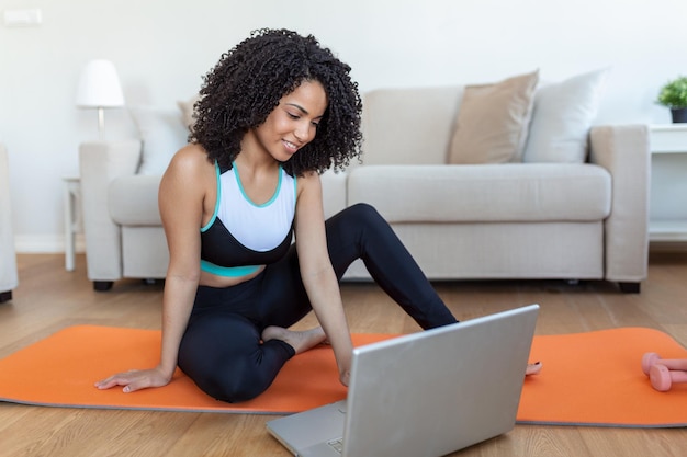 Jovem mulher se exercitando em casa em uma sala de estar Vídeo aula Jovem mulher repetindo exercícios enquanto assiste a sessão de treino online Linda jovem fazendo exercícios de fitness em casa