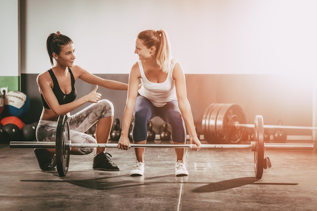 Jovem mulher se exercitando na academia com um personal trainer feminino.