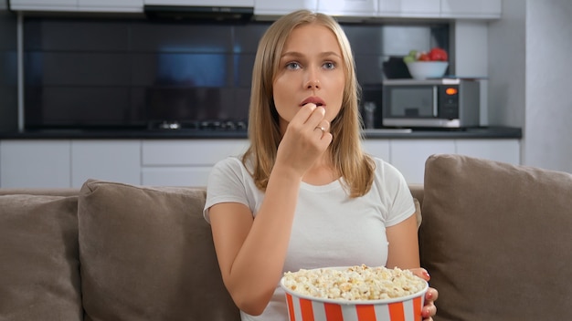 Jovem mulher segurando a caixa de pipoca e assistindo tv.