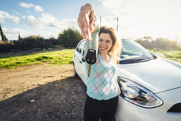 Jovem mulher segurando as chaves do carro novo e sorrindo para a câmera.