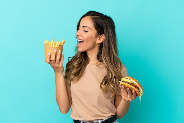 Jovem mulher segurando batatas fritas e hambúrguer sobre fundo isolado