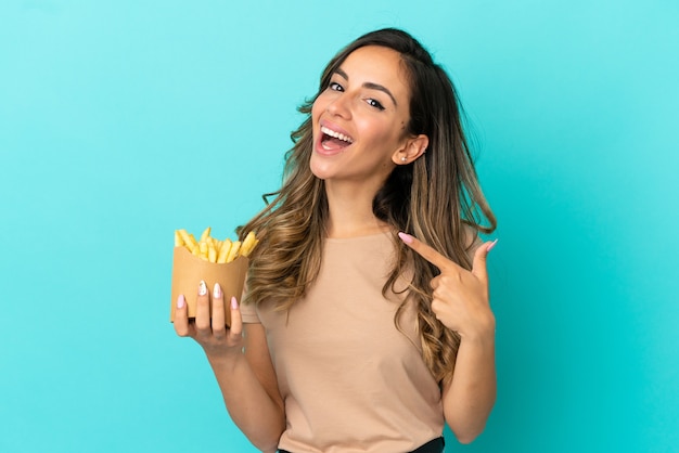 Jovem mulher segurando batatas fritas sobre um fundo isolado e fazendo um gesto de polegar para cima