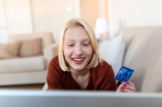 Jovem mulher segurando cartão de crédito e usando computador portátil Conceito de compras online Mulher feliz fazendo compras online em casa
