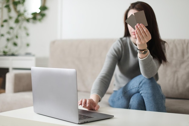 Jovem mulher segurando cartão de crédito e usando laptop em casa Pagando o conceito de loja eletrônica de internet banking para compras online em casa