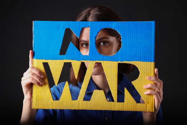 Foto jovem mulher segurando cartaz nas cores da bandeira ucraniana com palavras sem guerra em fundo preto