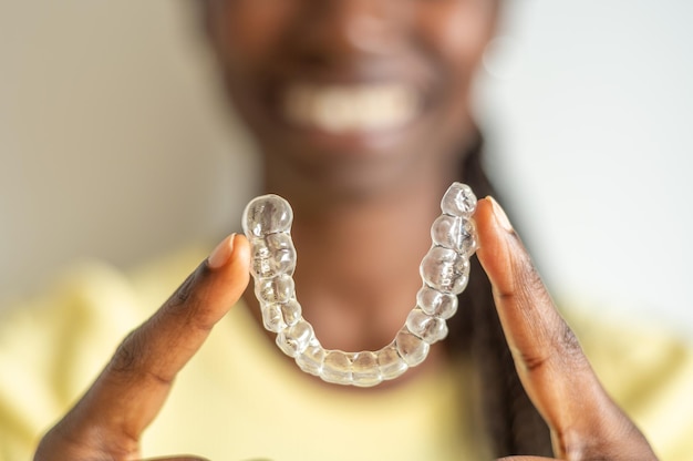 Jovem mulher segurando com dois dedos um alinhador dental invisível enquanto sorri