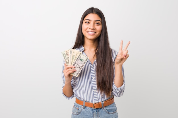 Jovem mulher segurando dólares mostrando o número dois com os dedos.