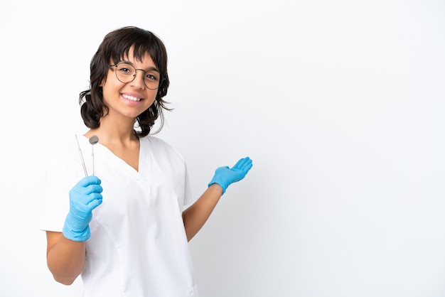 Jovem mulher segurando ferramentas isoladas em fundo branco, estendendo as mãos para o lado para convidar para vir