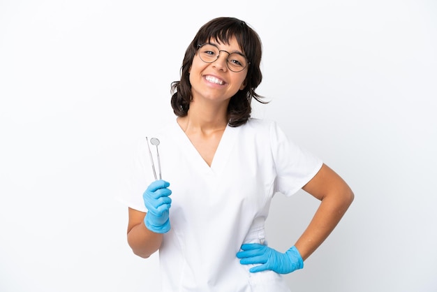 Jovem mulher segurando ferramentas isoladas em fundo branco posando com braços no quadril e sorrindo