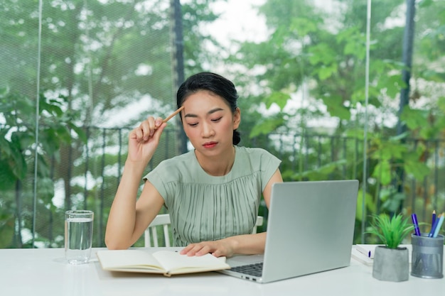 Jovem mulher segurando lápis pensando e planejando estratégia de negócios enquanto está sentado na mesa de escritório