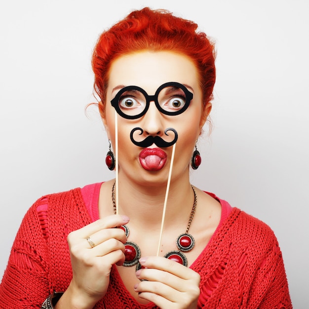 Jovem mulher segurando o bigode e óculos no palito.