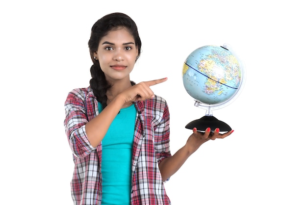 Jovem mulher segurando o globo do mundo e posando em uma parede branca.