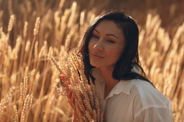Jovem mulher segurando o molho de espigas de trigo no campo agrícola.