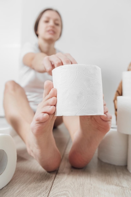 Jovem mulher segurando o rolo de papel higiênico pelos pés