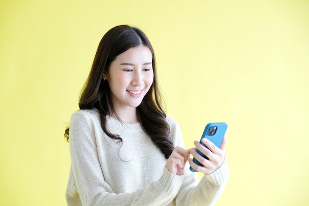 Foto jovem mulher segurando o telefone móvel sorrindo em pé sobre fundo amarelo isolado