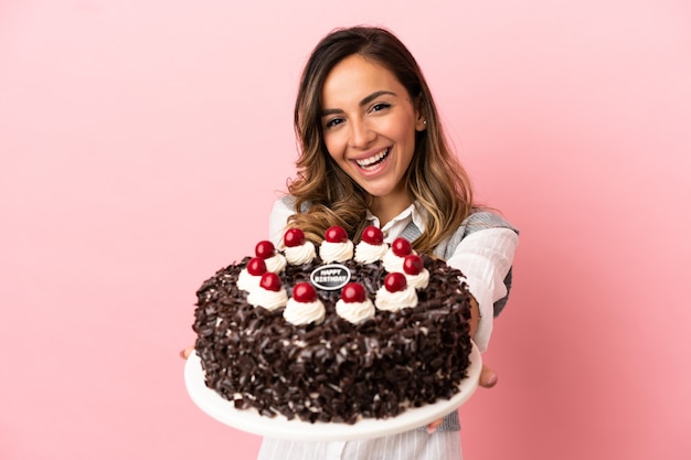 Jovem mulher segurando um bolo de aniversário sobre um fundo rosa isolado