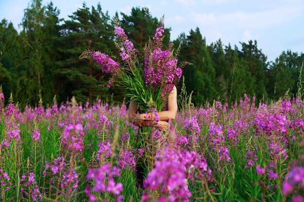 Jovem mulher segurando um buquê de flores cor de rosa em um campo a sorrir