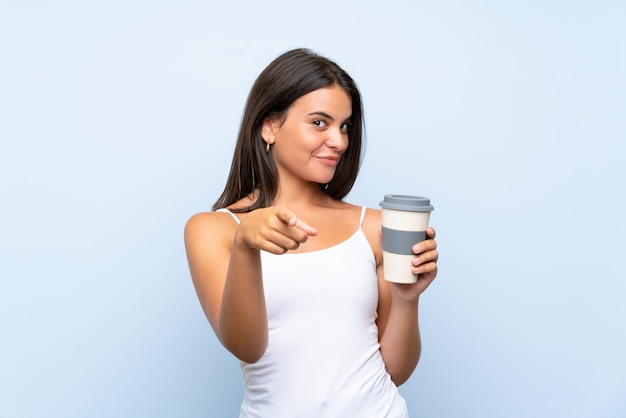Jovem mulher segurando um café para viagem, apontando com uma expressão confiante