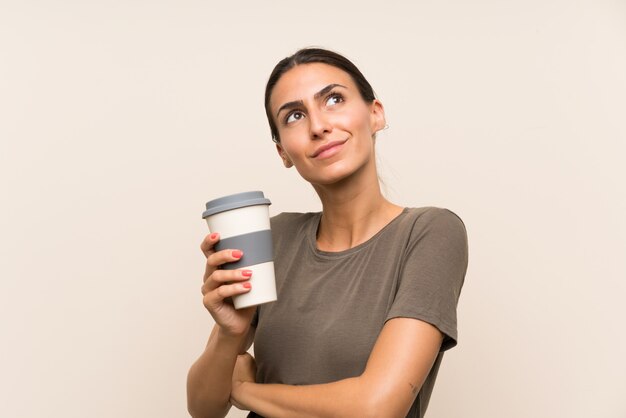 Jovem mulher segurando um café para viagem, olhando para cima enquanto sorrindo