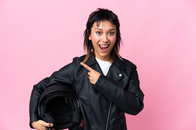 Jovem mulher segurando um capacete de moto sobre o dedo apontando rosa isolado para o lado