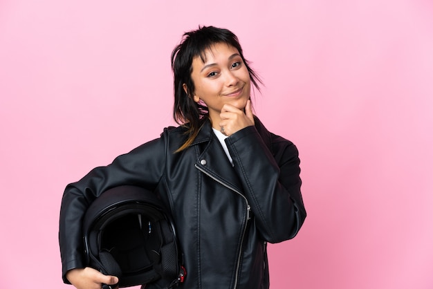 Jovem mulher segurando um capacete de moto sobre parede rosa rindo