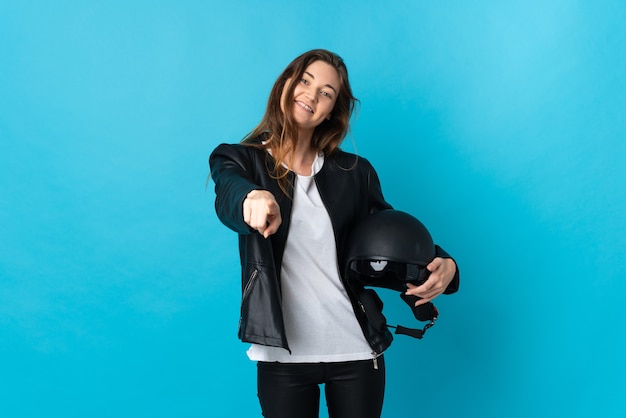Foto jovem mulher segurando um capacete de motociclista isolado na parede azul, apontando para a frente com uma expressão feliz