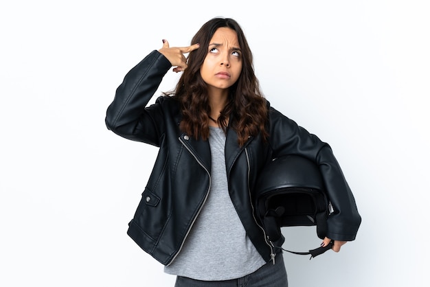 Jovem mulher segurando um capacete de motociclista sobre um branco isolado fazendo o gesto de loucura colocando o dedo na cabeça