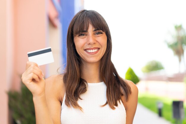 Jovem mulher segurando um cartão de crédito ao ar livre sorrindo muito
