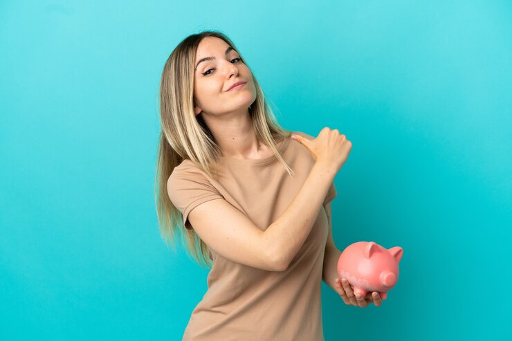 Foto jovem mulher segurando um cofrinho sobre um fundo azul isolado, orgulhosa e satisfeita