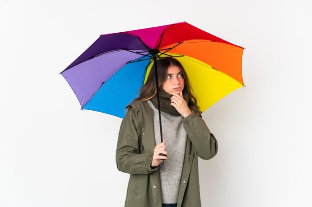 Jovem mulher segurando um guarda-chuva isolado na parede branca, tendo dúvidas