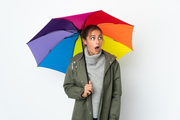 Jovem mulher segurando um guarda-chuva isolado no fundo branco, olhando para cima e com expressão de surpresa