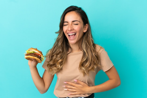 Jovem mulher segurando um hambúrguer sobre um fundo isolado e sorrindo muito