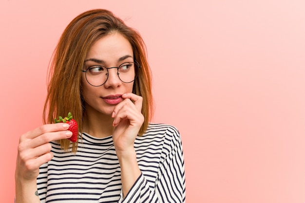 Jovem mulher segurando um morango relaxado pensando em algo