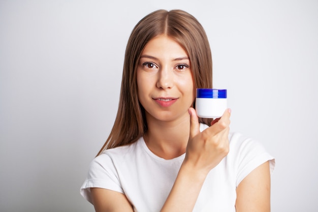 Jovem mulher segurando um pote de creme para cuidados com a pele