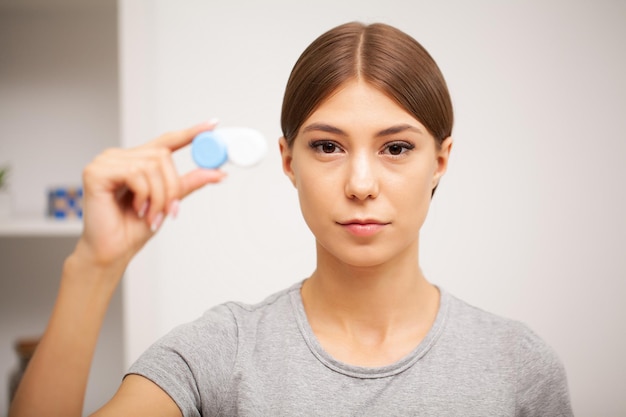 Jovem mulher segurando um recipiente branco com lentes