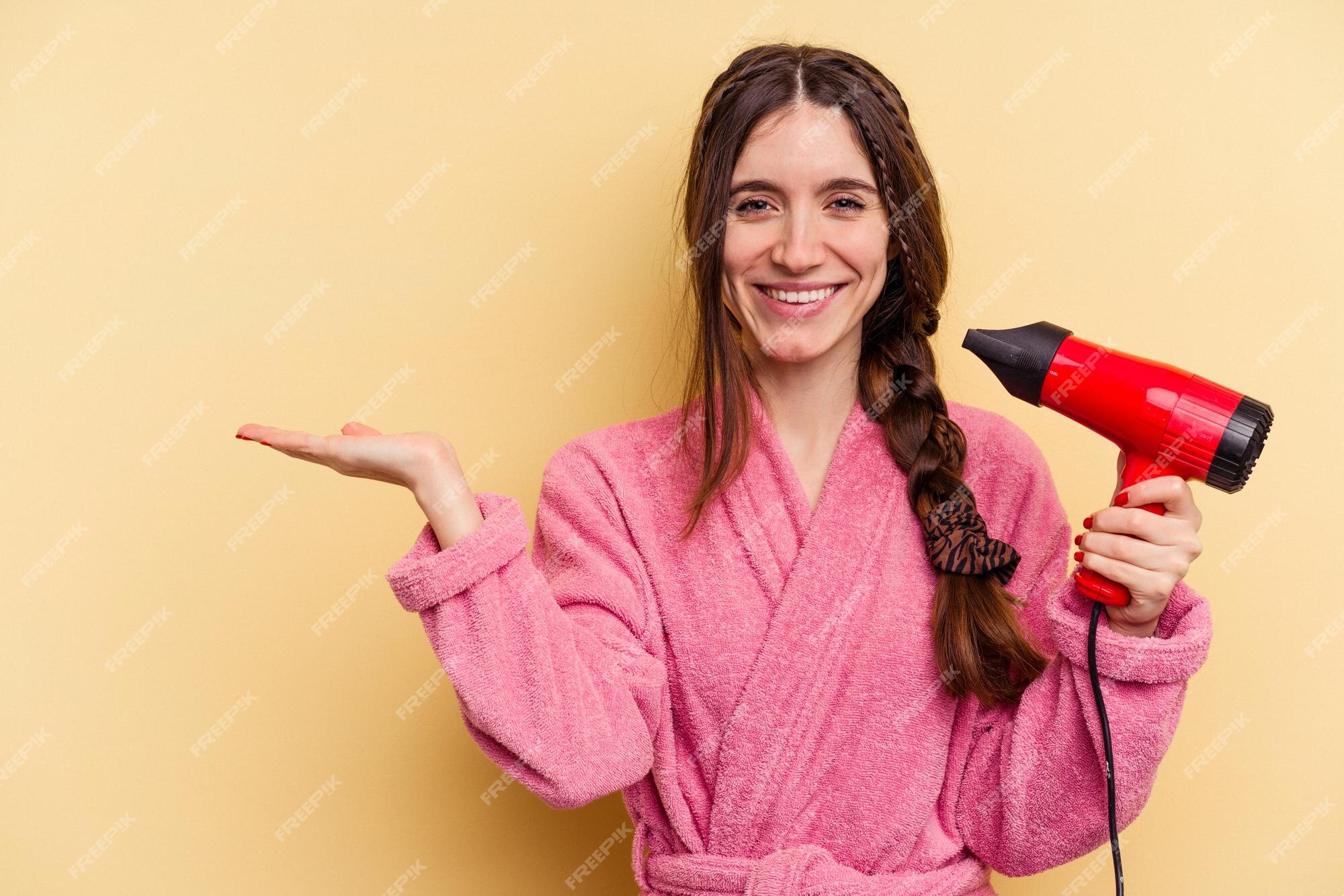 Secador de cabelo preto na mão de uma mulher em um fundo amarelo