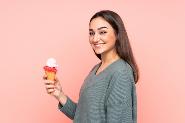 Jovem mulher segurando um sorvete de corneta isolado na parede rosa sorrindo muito