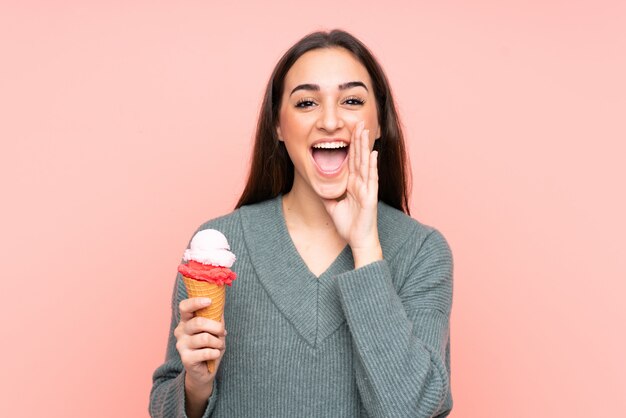 Jovem mulher segurando um sorvete de corneta na rosa gritando com a boca aberta