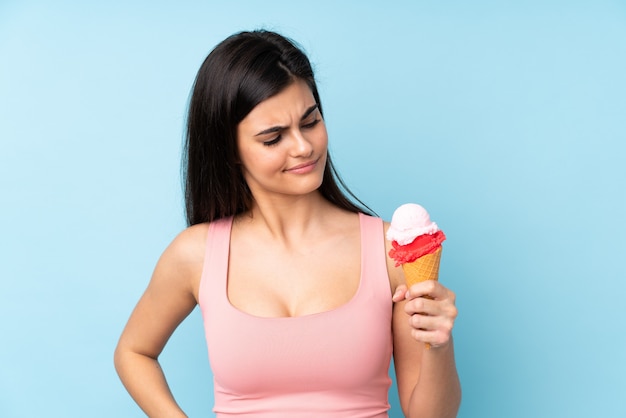Jovem mulher segurando um sorvete de corneta sobre parede azul com expressão triste