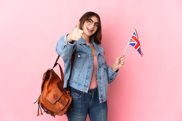 Jovem mulher segurando uma bandeira do Reino Unido isolada em rosa com o polegar para cima porque algo bom aconteceu