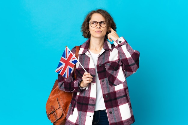 Jovem mulher segurando uma bandeira do Reino Unido isolada, tendo dúvidas e pensando