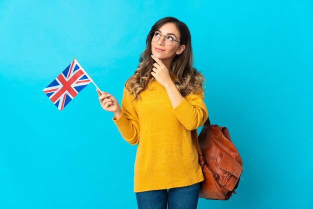 Jovem mulher segurando uma bandeira do Reino Unido posando isolada contra a parede em branco