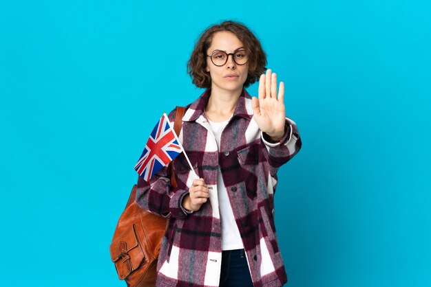 Jovem mulher segurando uma bandeira do Reino Unido posando isolada contra a parede em branco