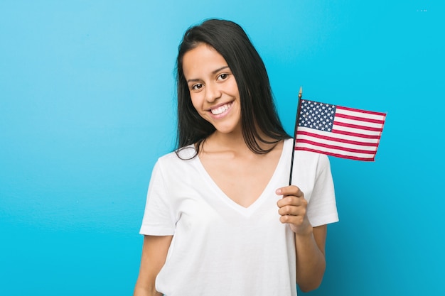 Jovem mulher segurando uma bandeira dos Estados Unidos feliz, sorridente e alegre