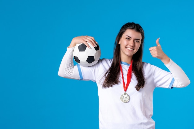 Jovem mulher segurando uma bola de futebol na parede azul de frente