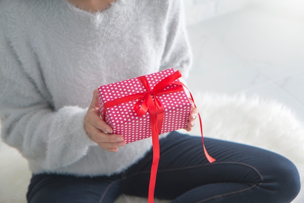 jovem mulher segurando uma caixa de presente com fita vermelha.