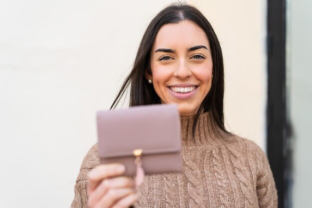 Foto jovem mulher segurando uma carteira ao ar livre com expressão feliz